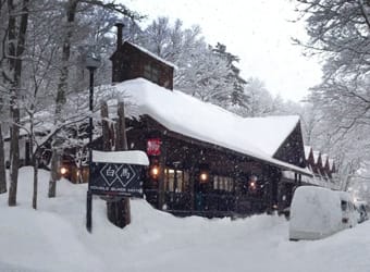 Snow-covered cabin with lit windows amidst a snowy landscape.