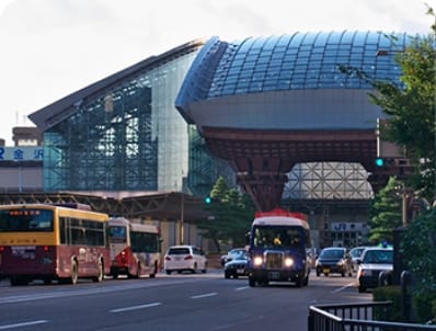 Modern glass building with a curved roof beside a street with buses and cars.