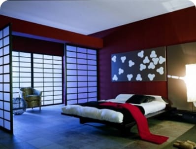A modern bedroom with red walls, a black bed, white bedding, red throw, and shoji screen windows.