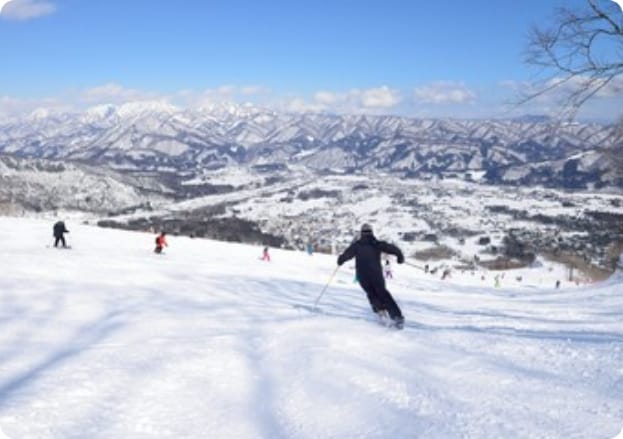 Skiers on a snowy mountain slope with scenic views of hills and clear skies.
