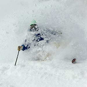A skier submerged in deep snow with only part of their head and one arm visible.